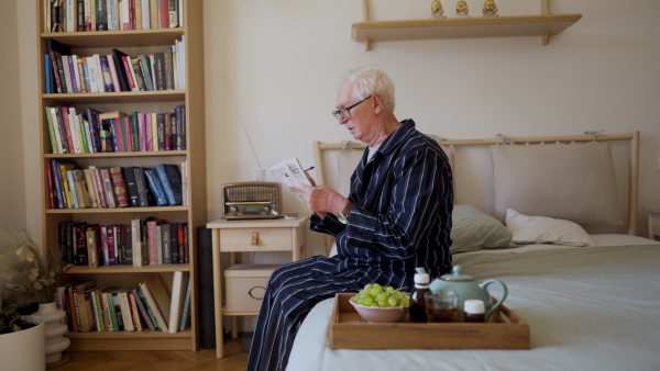 Video of a senior man sitting in bed at the morning and doing crosswords.