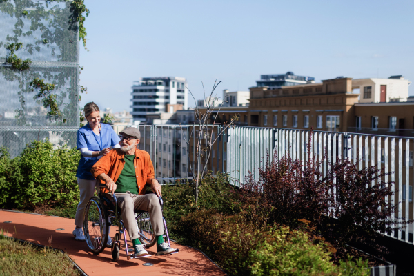 Nurse pushing senior man in a wheelchair. Female caregiver and elderly man enjoying a warm autumn day in nursing home, residential care home.