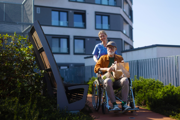 Nurse pushing senior man in a wheelchair. Female caregiver and elderly man enjoying a warm spring, autumn day in nursing home, residential care home.