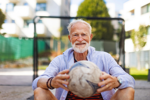 Senior man holding football, ball in his hands. Older, vital man has active lifestyle, doing sport every day.