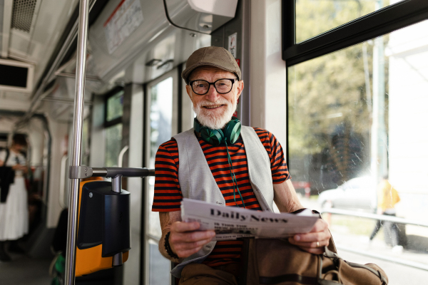 Elderly man traveling through the city by bus, reading a newspaper. Senior city commuter taking tram to grocery store, using public transportation.