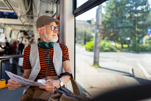 Elderly man traveling through the city by bus, reading a newspaper. Senior city commuter taking tram to grocery store, using public transportation.