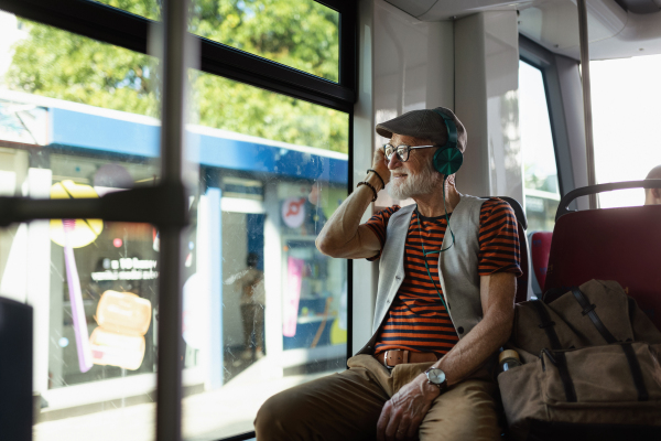 An elderly man traveling through the city by bus, listening music via modern headphones. Senior city commuter taking tram to grocery, using public transportation.