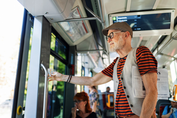 Elderly man traveling through the city by bus, standing by door. Senior city commuter taking tram to grocery store, using public transportation.