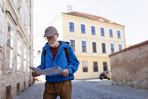 Senior tourist exploring a new city, interesting places. Elderly man holding a paper map and looking for the route. Solo traveling and trips in retirement.