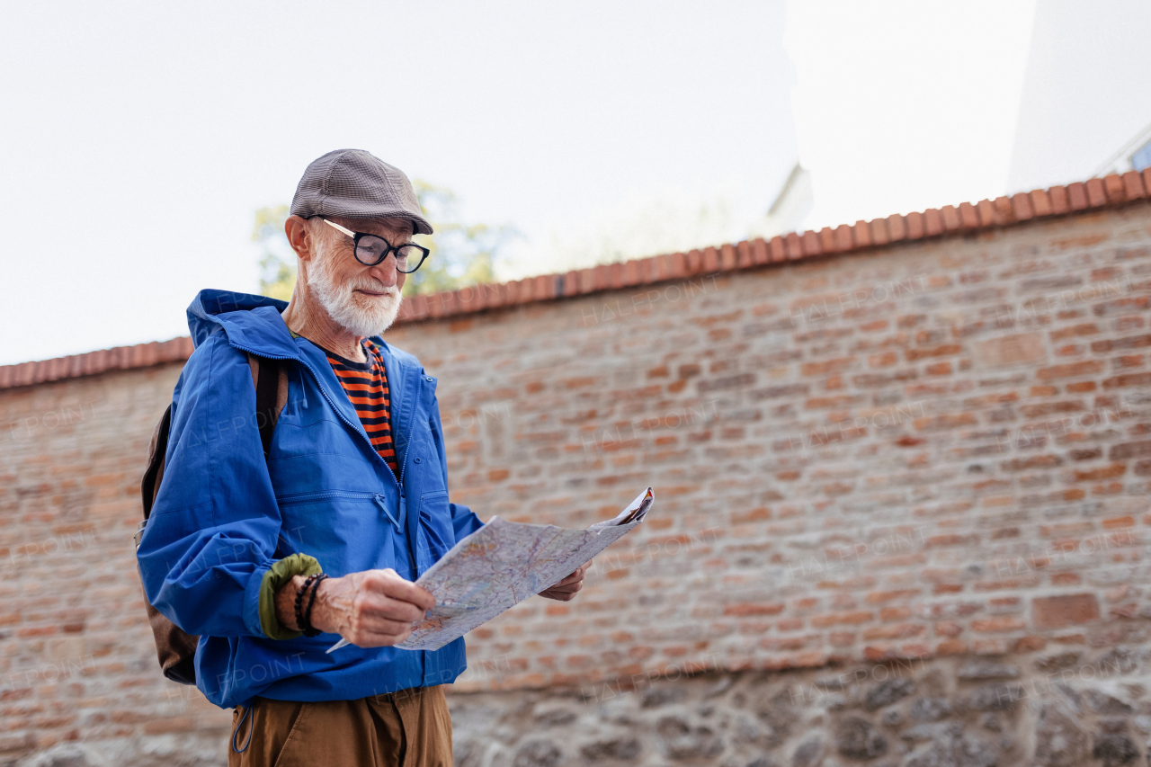 Senior tourist exploring a new city, interesting places. Elderly man holding a paper map and looking for the route. Solo traveling and trips in retirement.