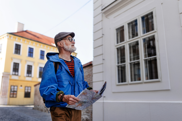 Senior tourist exploring a new city, interesting places. Elderly man holding a paper map and looking for the route. Solo traveling and trips in retirement.