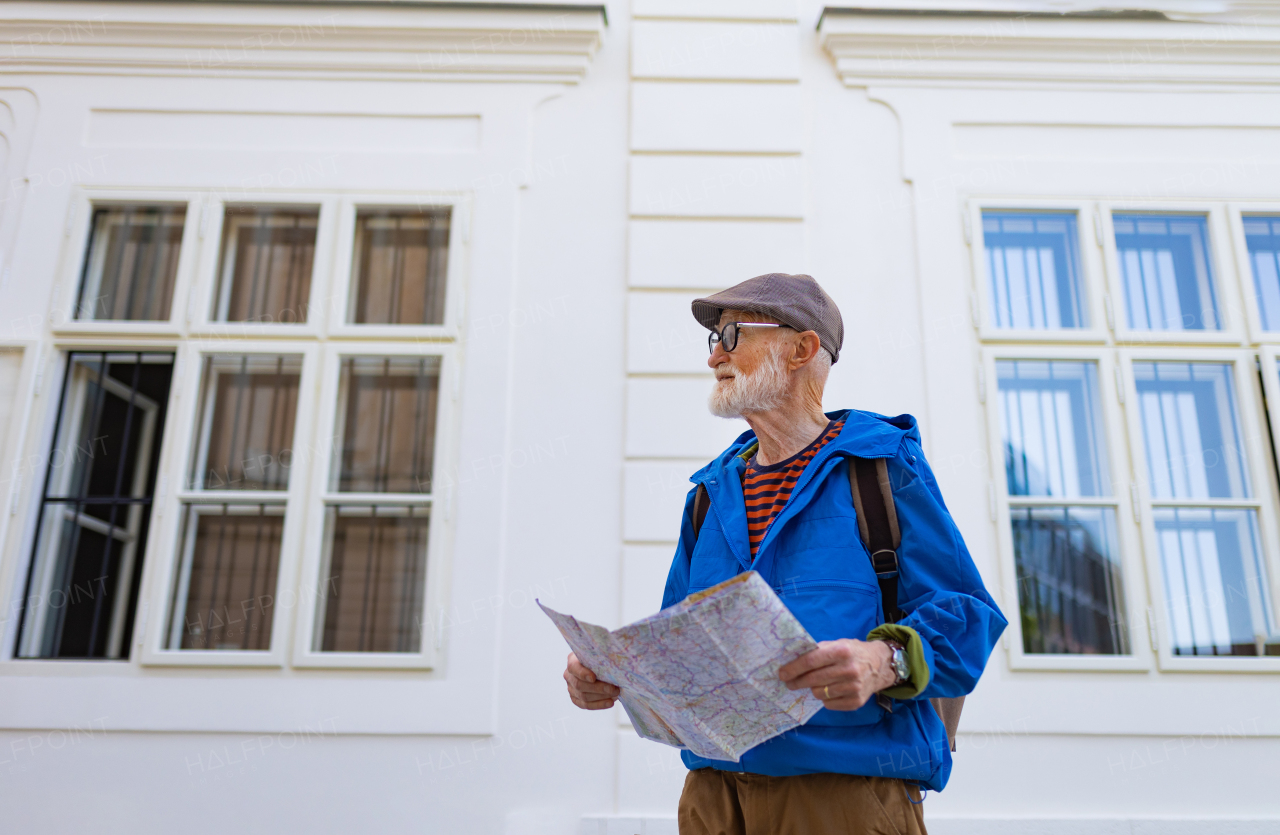 Senior tourist exploring a new city, interesting places. Elderly man holding a paper map and looking for the route. Solo traveling and trips in retirement.