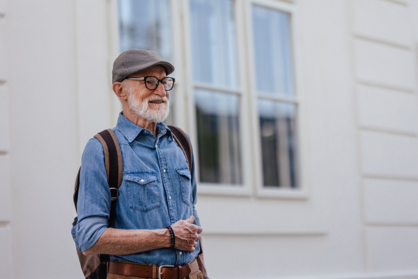 Portrait of handsome senior man in the city. An elderly independent man with backpack visiting new city. Traveling and solo trips in retirement.