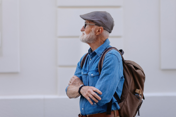 Portrait of handsome senior man in the city. An elderly independent man with backpack visiting new city. Traveling and solo trips in retirement.