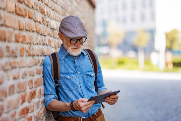 Side view of senior tourist exploring a new city, interesting places. Elderly man holding tablet, looking for the route. Traveling and solo trips in retirement.