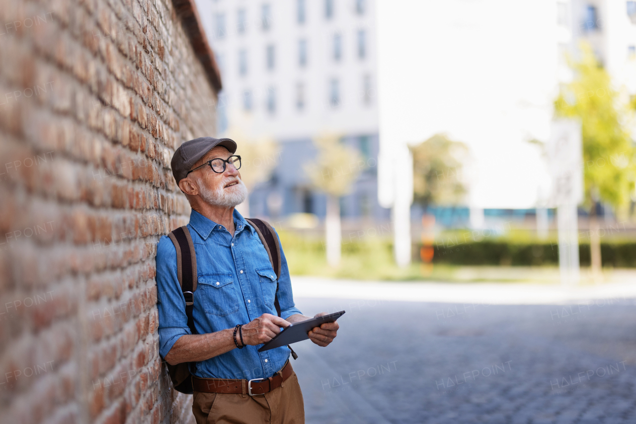 Side view of senior tourist exploring a new city, interesting places. Elderly man holding tablet, looking for the route. Traveling and solo trips in retirement.