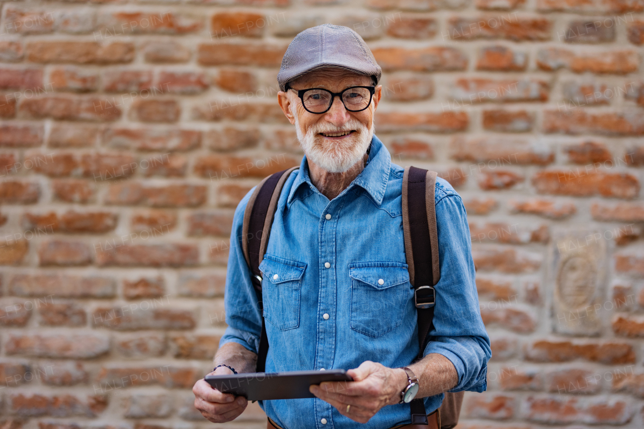 Side view of senior tourist exploring a new city, interesting places. Elderly man holding tablet, looking for the route. Traveling and solo trips in retirement.