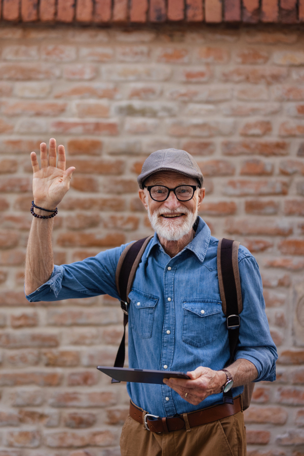 Side view of senior tourist exploring a new city, interesting places. Elderly man holding tablet, looking for the route. Traveling and solo trips in retirement.