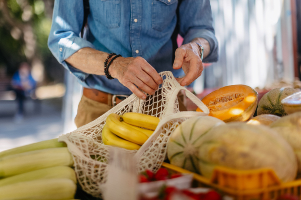 Portrait of senior man shopping at market in the city. Elderly man buying fresh vegetables and fruits from market stall.