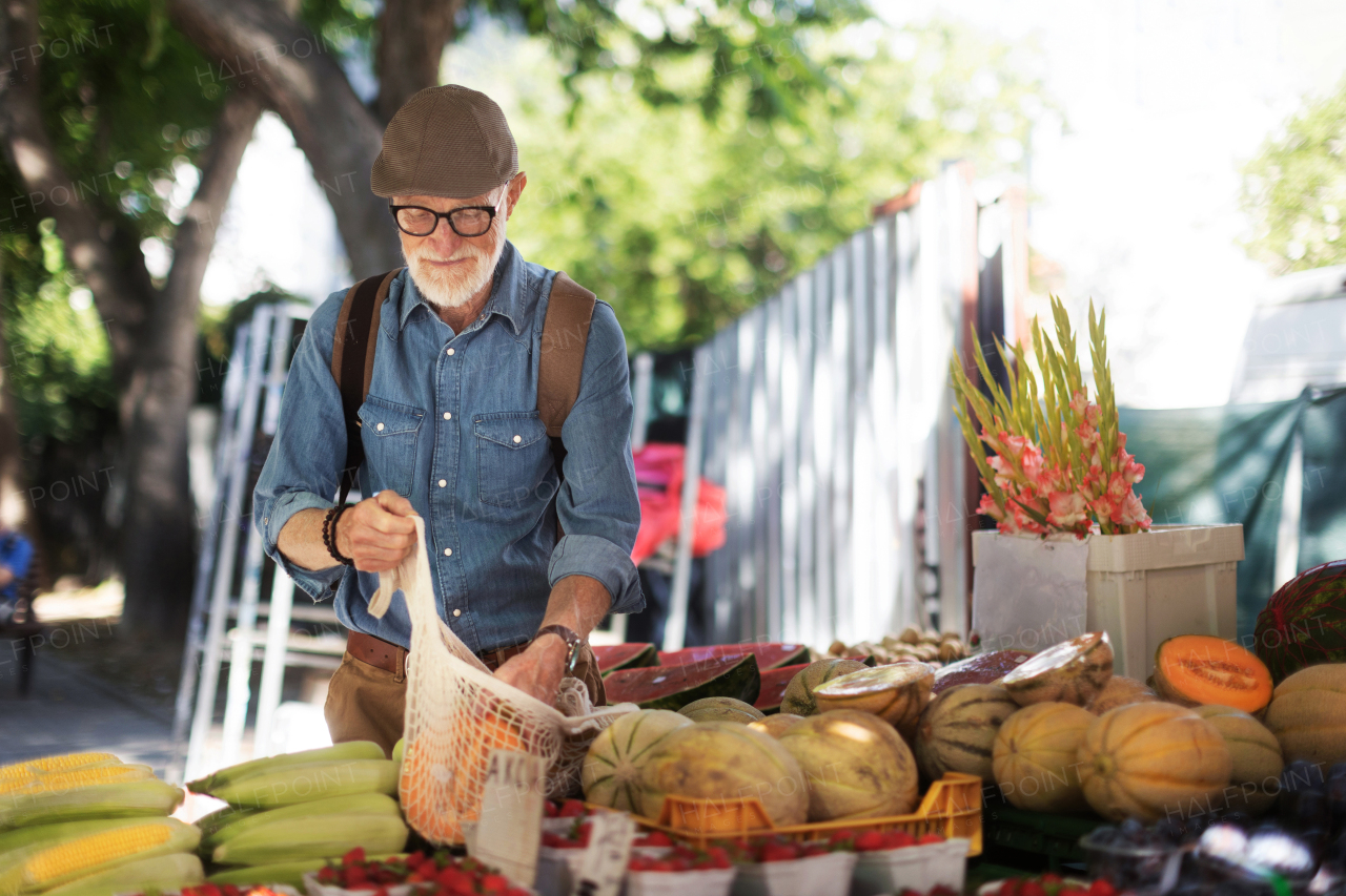 Portrait of senior man shopping at market in the city. Elderly man buying fresh vegetables and fruits from market stall.