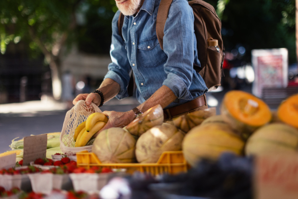 Portrait of senior man shopping at market in the city. Elderly man buying fresh vegetables and fruits from market stall.