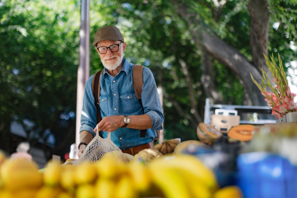 Portrait of senior man shopping at market in the city. Elderly man buying fresh vegetables and fruits from market stall.