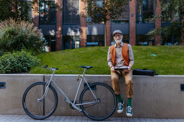 Stylish senior man sitting in the city park, holding tablet, shopping online. Concept of digital literacy, seniors using digital technologies.