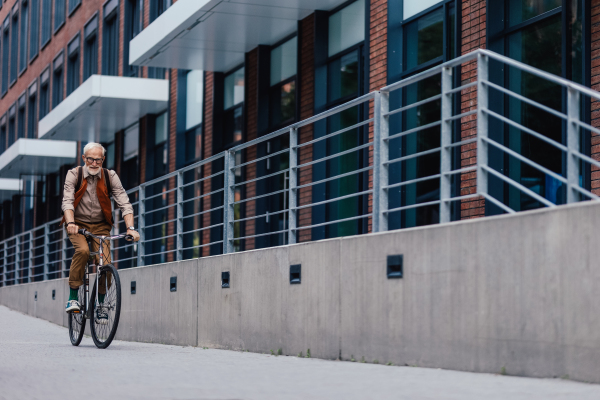 An elderly man, cyclist traveling through the city by bike. Senior city commuter riding a bike to grocery store.