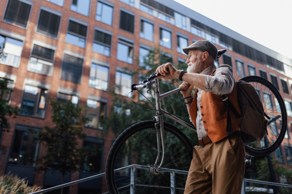 An elderly man, cyclist traveling through the city by bike, carrying bicycle on shoulder. Senior city commuter riding a bike.