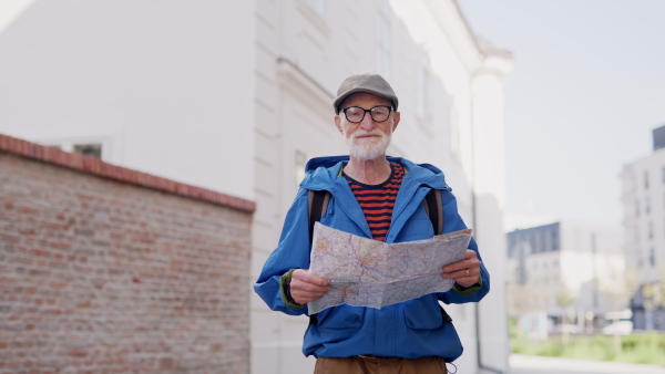 Senior tourist exploring a new city, interesting places. Elderly man holding a paper map and looking for the route. Solo traveling and trips in retirement.