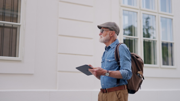 Side view of senior tourist exploring a new city, interesting places. Elderly man holding tablet, looking for the route. Traveling and solo trips in retirement.