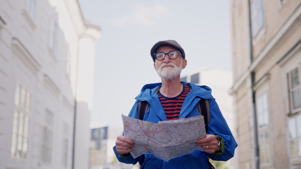 Senior tourist exploring a new city, interesting places. Elderly man holding a paper map and looking for the route. Solo traveling and trips in retirement.