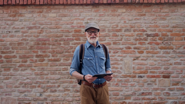 Side view of senior tourist exploring a new city, interesting places. Elderly man holding tablet, looking for the route. Traveling and solo trips in retirement.