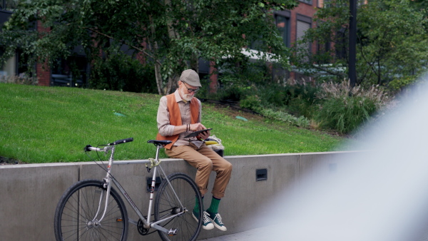 Stylish senior man sitting in the city park, listening to music via wireless headphones. Concept of old man young at heart.