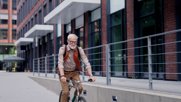 An elderly man, cyclist traveling through the city by bike. Vital senior city commuter riding a bike, exercising.