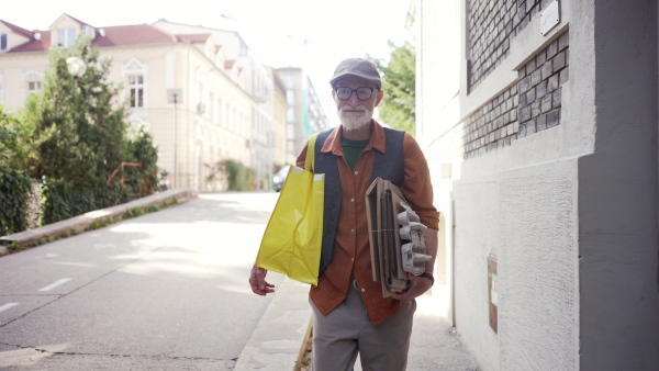 A senior man going to throw paper waste, cardboard into recycling container in front his apartment complex. Elderly man sorting the waste according to material into colored bins.