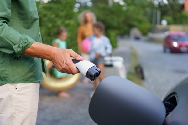 A man holding power supply cable while his family waiting for car charging at electric vehicle charging station, closeup