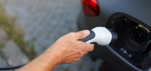 A man holding power supply cable at electric vehicle charging station, closeup