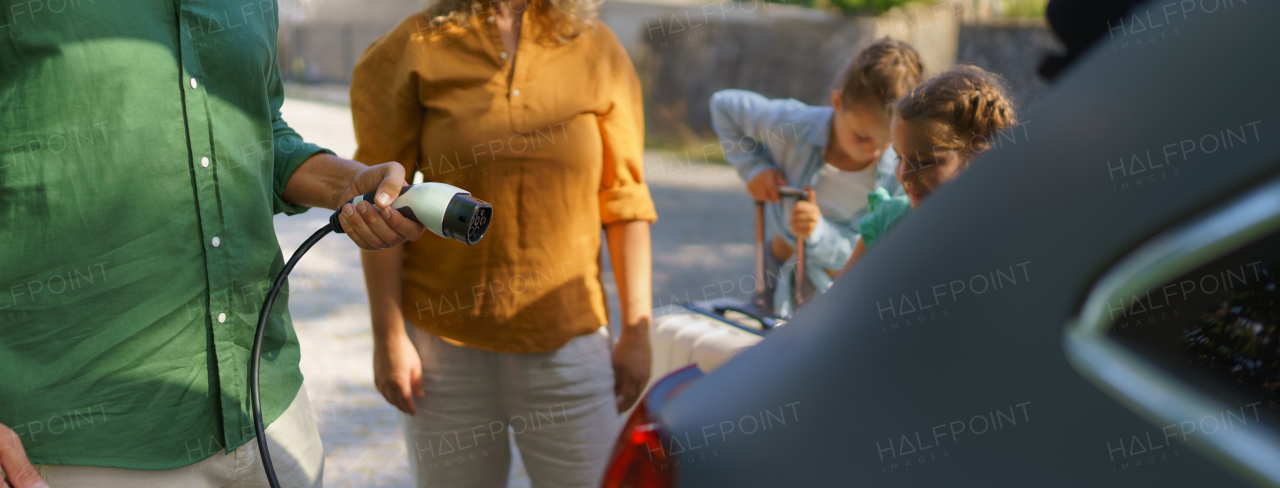 A man holding power supply cable while his family waiting for car charging at electric vehicle charging station, closeup