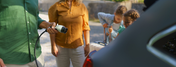 A man holding power supply cable while his family waiting for car charging at electric vehicle charging station, closeup