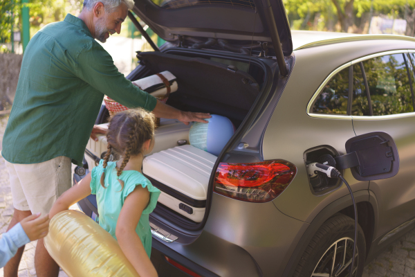 A fmily with little children loading car and waiting for charging car before going on picnic.