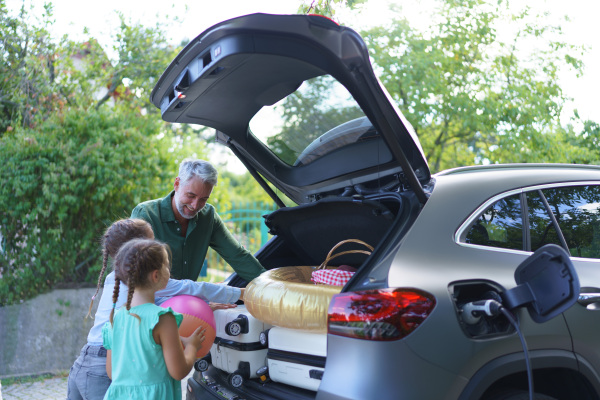 A fmily with little children loading car and waiting for charging car before going on picnic.