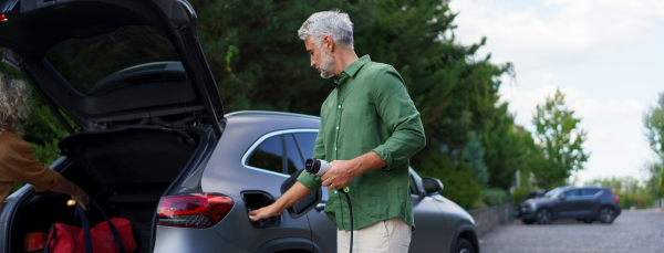 A man holding power supply cable at electric vehicle charging station, closeup