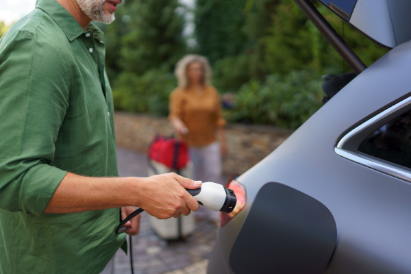 A man holding power supply cable while his wife waiting for car charging at electric vehicle charging station, closeup