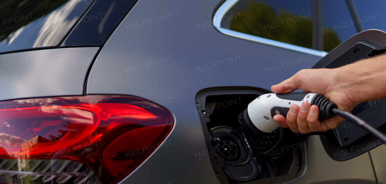 A man holding power supply cable at electric vehicle charging station, closeup