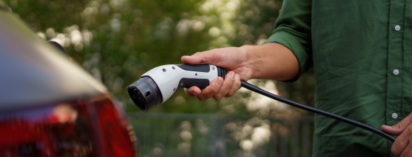 A man holding power supply cable at electric vehicle charging station, closeup