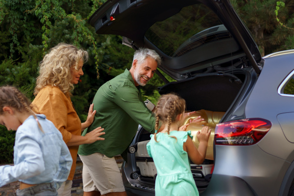 Happy family preparing for a holiday, putting suitcases in a car trunk, while their electric car charging.