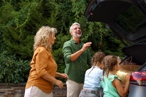 Young family giving their luggage in to a car trunk, preparing for holiday.