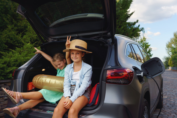 Cute little girls sitting in a boot while waiting for charging car before travelling on summer holiday.