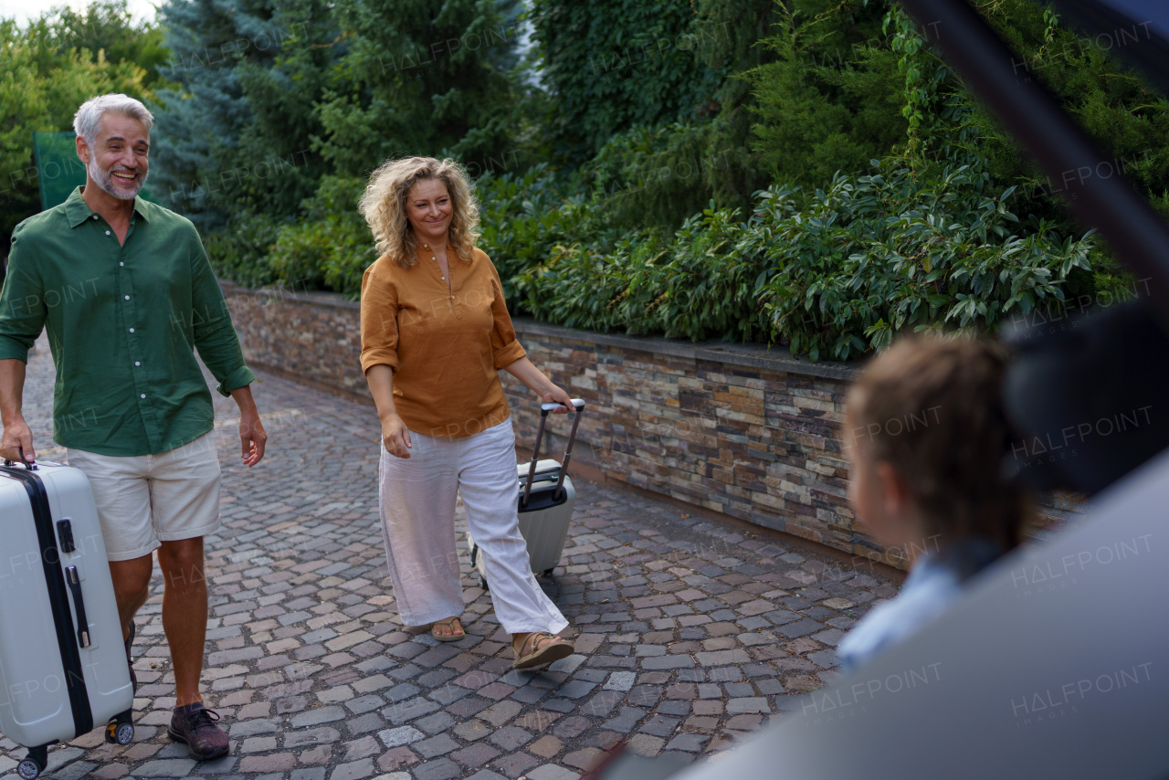 Happy family preparing for a holiday, putting suitcases in a car trunk.