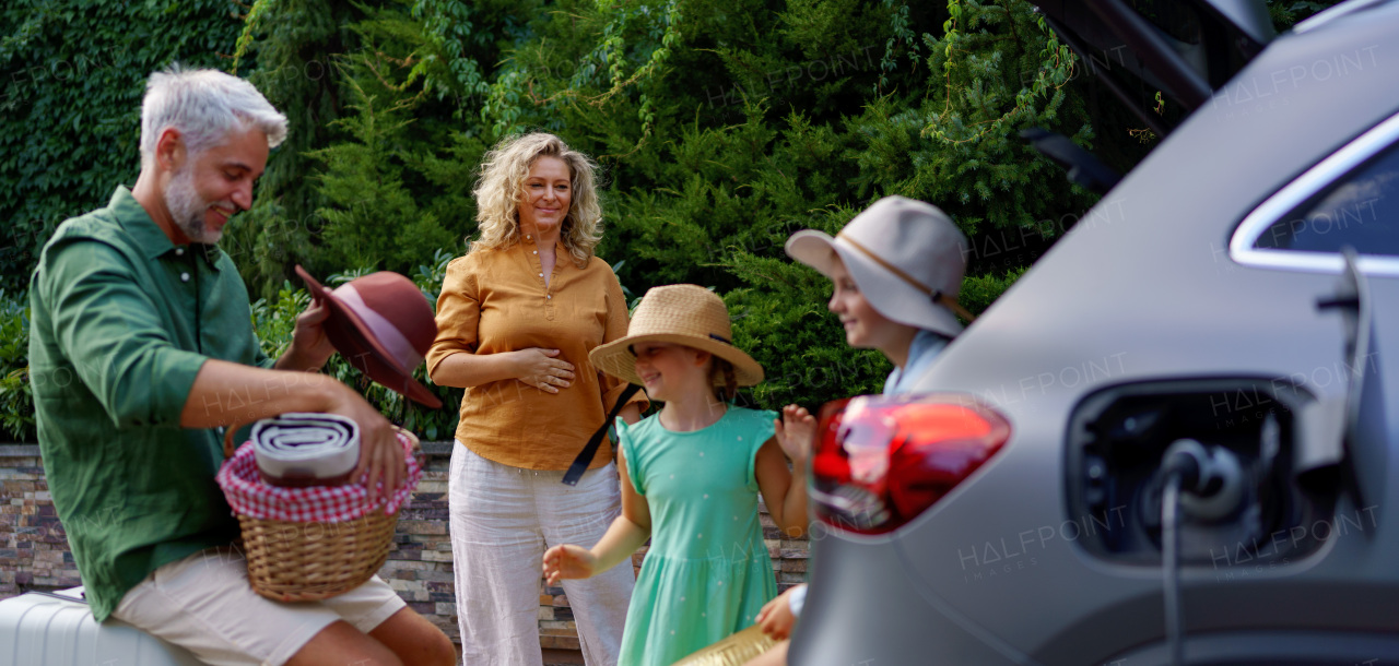 A fmily with little children loading car and waiting for charging car before going on picnic.