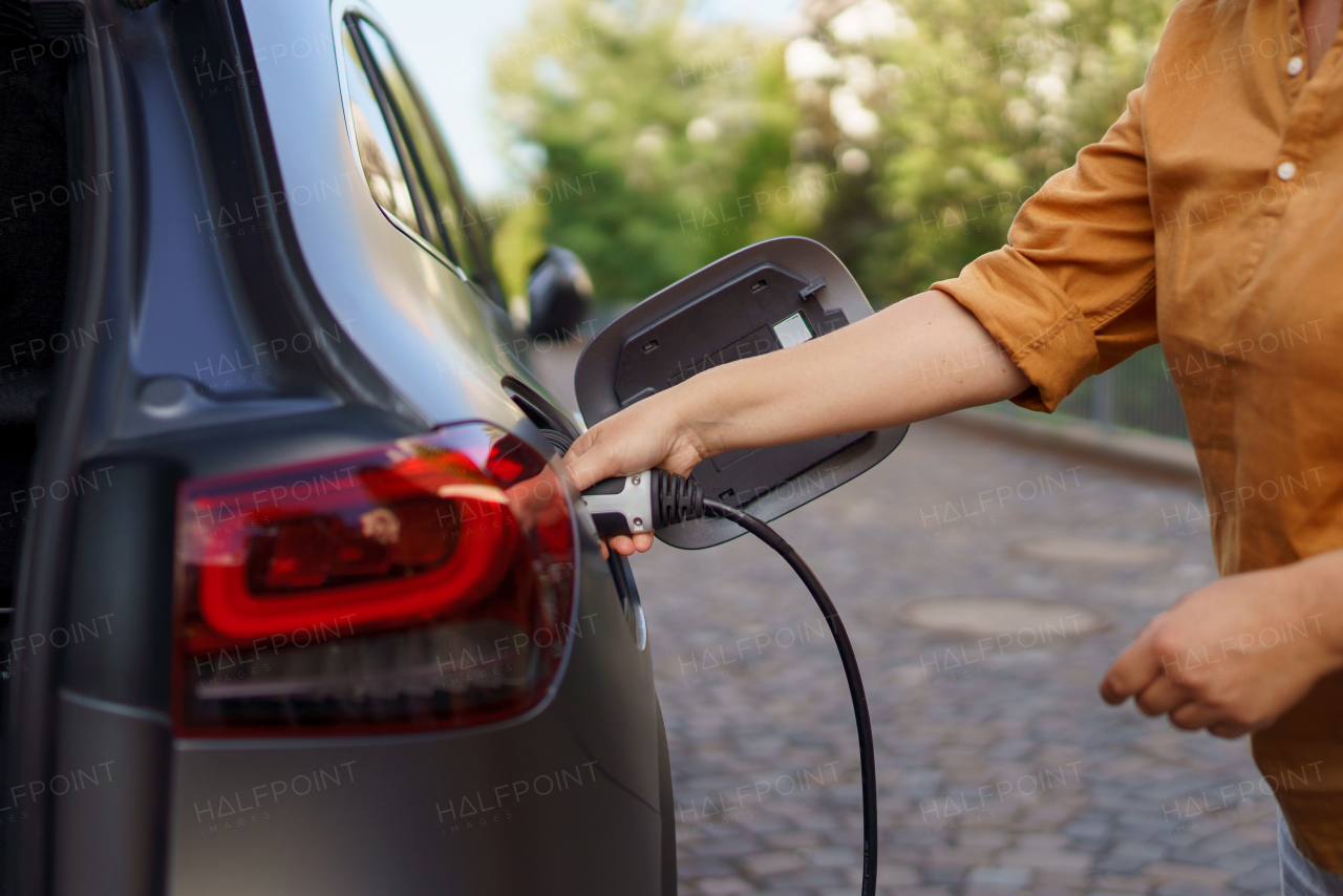 A woman holding power supply cable at electric vehicle charging station, closeup