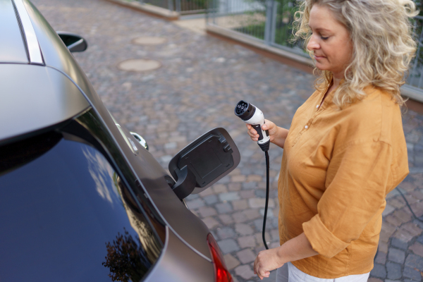 A woman holding power supply cable at electric vehicle charging station, closeup