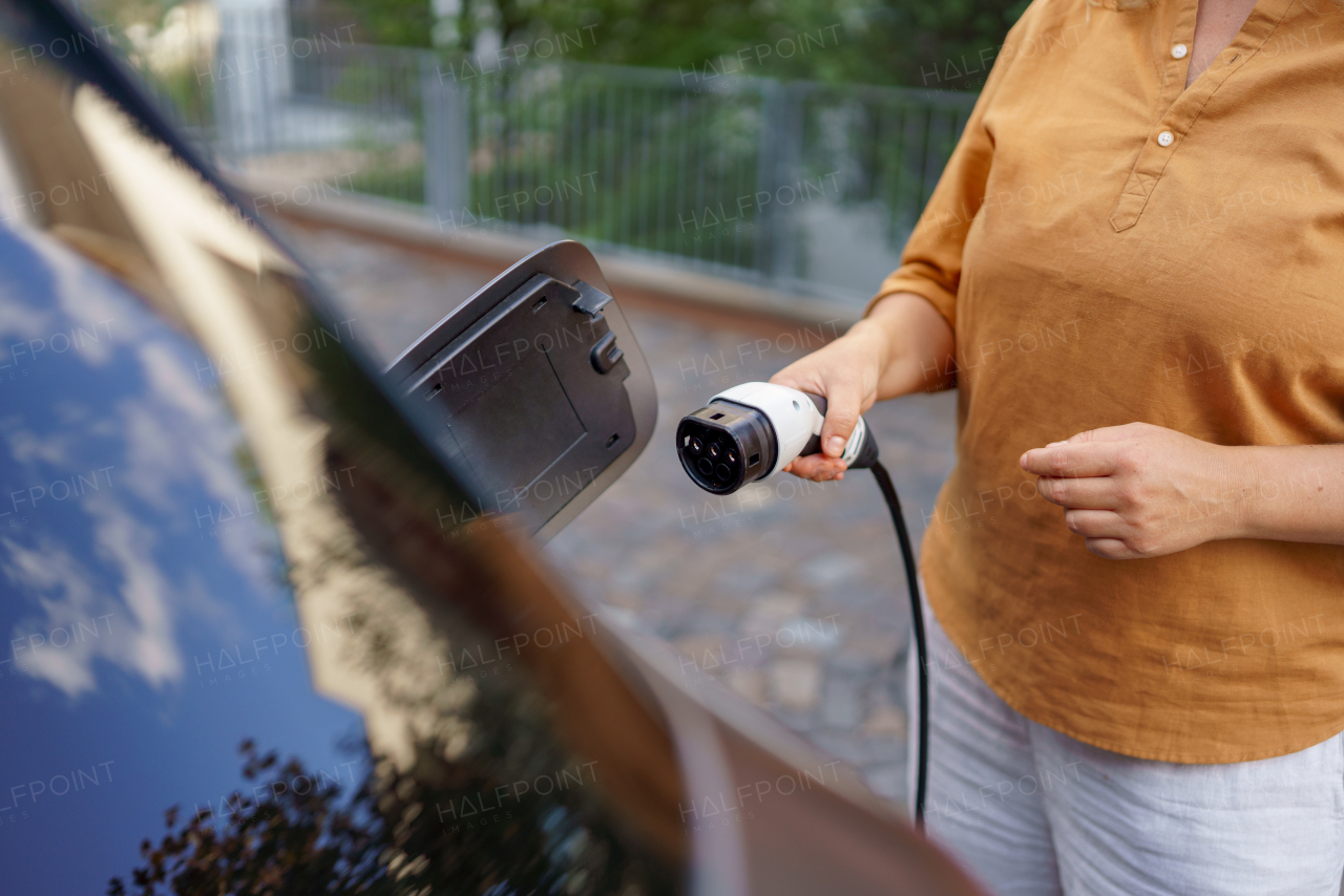 A woman holding power supply cable at electric vehicle charging station, closeup